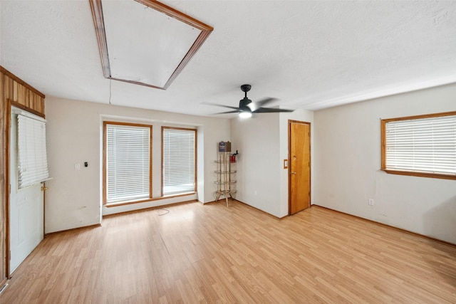 unfurnished room featuring attic access, light wood finished floors, ceiling fan, and a textured ceiling
