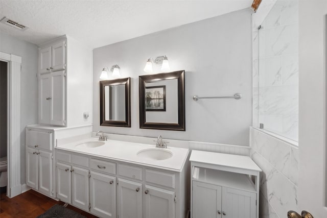 full bath featuring a sink, a textured ceiling, double vanity, and visible vents