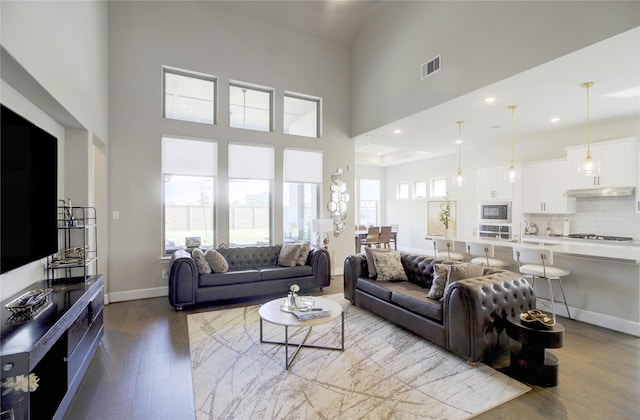 living room with baseboards, a high ceiling, visible vents, and wood finished floors