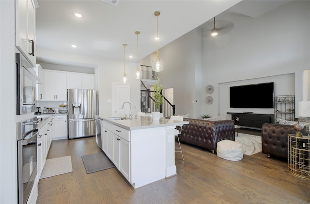 kitchen featuring appliances with stainless steel finishes, a sink, light countertops, wood finished floors, and a kitchen bar