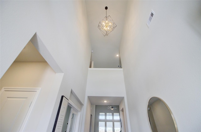 foyer with visible vents, a towering ceiling, and ceiling fan with notable chandelier