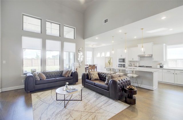 living room featuring visible vents, wood finished floors, baseboards, a high ceiling, and recessed lighting