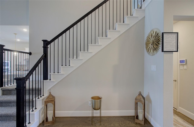 stairway featuring baseboards, wood finished floors, and a high ceiling