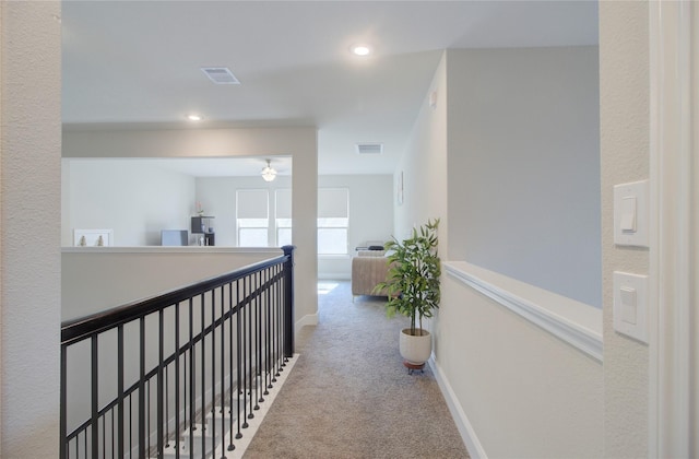 hallway with carpet floors, baseboards, visible vents, and an upstairs landing