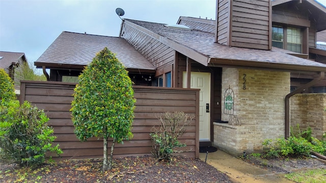 view of property exterior featuring brick siding, roof with shingles, and fence