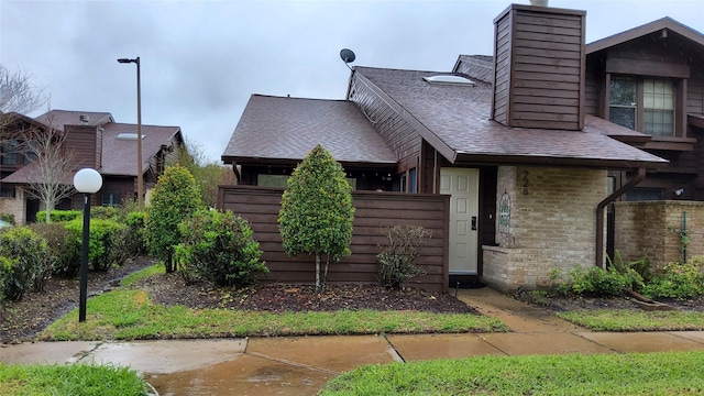 view of front of house with brick siding, fence, a chimney, and a shingled roof