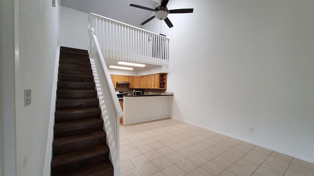 stairs featuring a ceiling fan, a high ceiling, baseboards, and tile patterned flooring
