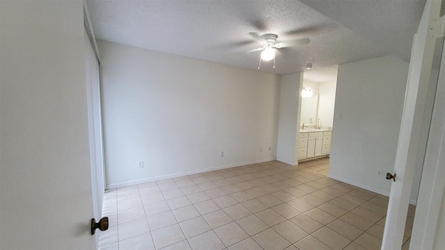 empty room featuring baseboards, a ceiling fan, a textured ceiling, and light tile patterned flooring