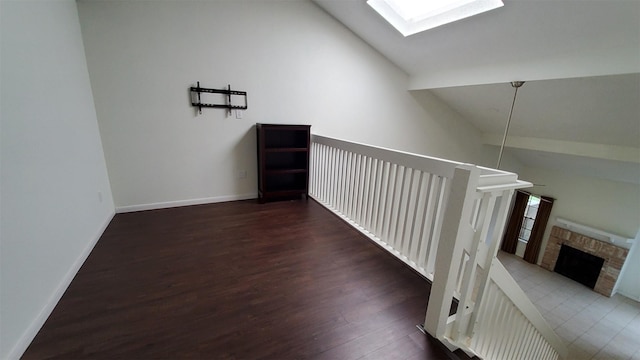 hallway featuring baseboards, a skylight, wood finished floors, and high vaulted ceiling