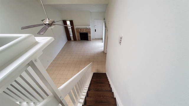 stairs with a brick fireplace, a ceiling fan, and vaulted ceiling