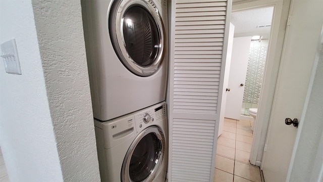 laundry area with stacked washer and dryer, laundry area, and light tile patterned flooring