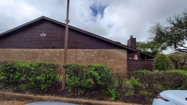 view of home's exterior featuring fence, a chimney, and brick siding