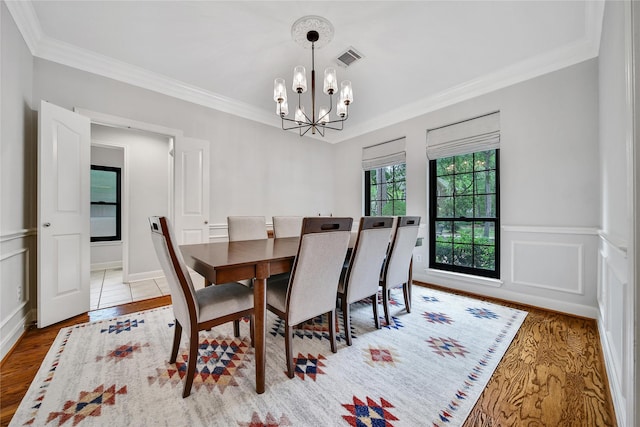 dining room with visible vents, ornamental molding, wood finished floors, a wainscoted wall, and a notable chandelier