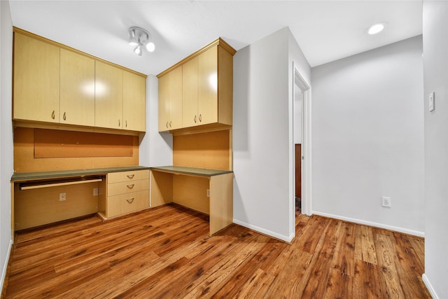 unfurnished office featuring baseboards, wood finished floors, and built in study area