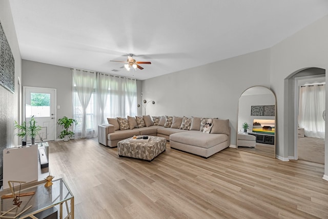 living area featuring arched walkways, ceiling fan, and light wood finished floors