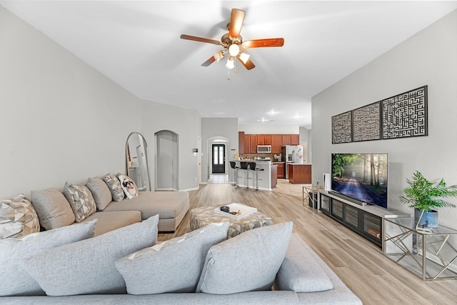 living room featuring light wood-style floors, arched walkways, baseboards, and ceiling fan