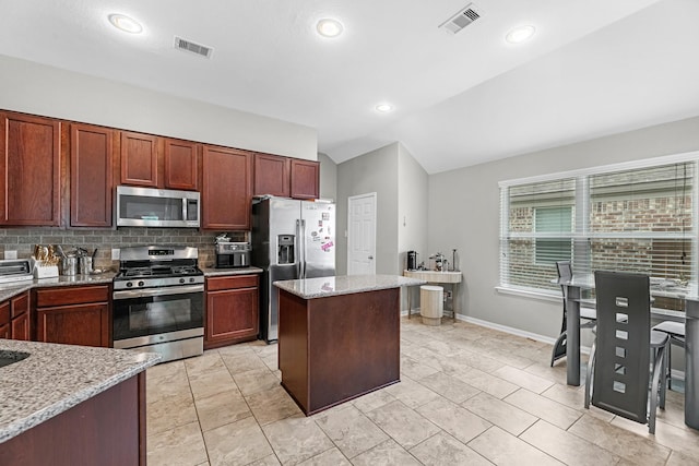 kitchen featuring appliances with stainless steel finishes, lofted ceiling, light stone counters, and visible vents