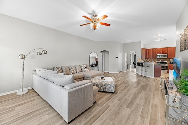 living area featuring baseboards, arched walkways, light wood-style flooring, and a ceiling fan