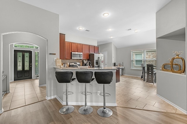 kitchen featuring decorative backsplash, a peninsula, a breakfast bar, brown cabinets, and appliances with stainless steel finishes