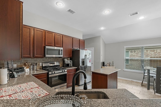 kitchen with appliances with stainless steel finishes, light stone counters, a sink, backsplash, and visible vents
