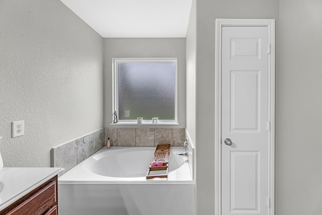 bathroom featuring a textured wall, a garden tub, and vanity