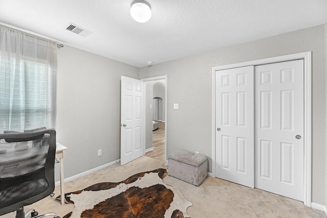 bedroom featuring visible vents, arched walkways, baseboards, a closet, and light carpet