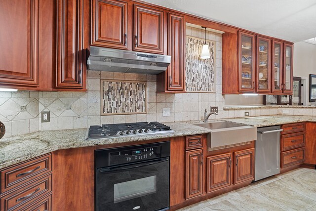 28710 Sapphire Cir, Magnolia, TX 77355 - kitchen featuring appliances with stainless steel finishes, under cabinet range hood, a sink, light stone counters, and tasteful backsplash