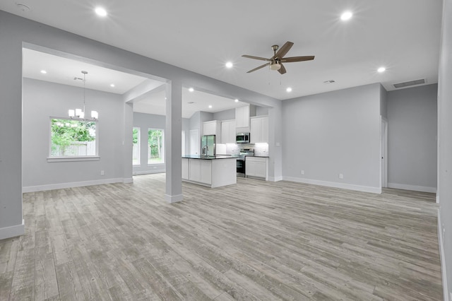 12390 Green Ridge Dr, Willis, TX 77318 - unfurnished living room with visible vents, light wood-style flooring, ceiling fan with notable chandelier, and baseboards