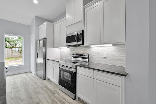 12390 Green Ridge Dr, Willis, TX 77318 - kitchen with white cabinets, light wood-style flooring, dark stone counters, stainless steel appliances, and decorative backsplash