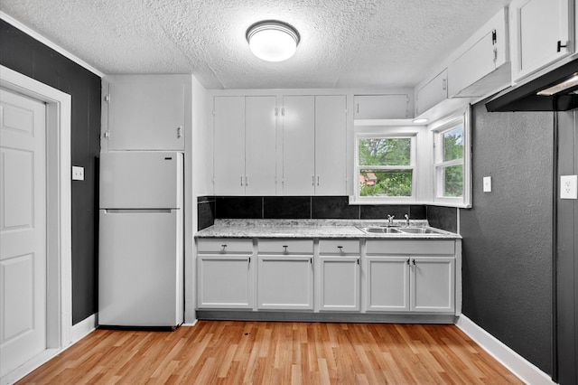 kitchen featuring white cabinets, freestanding refrigerator, light wood-type flooring, and a textured ceiling