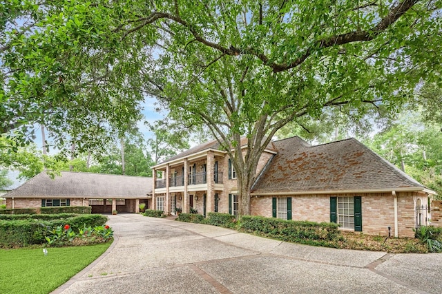 greek revival inspired property with brick siding, a shingled roof, a balcony, and concrete driveway