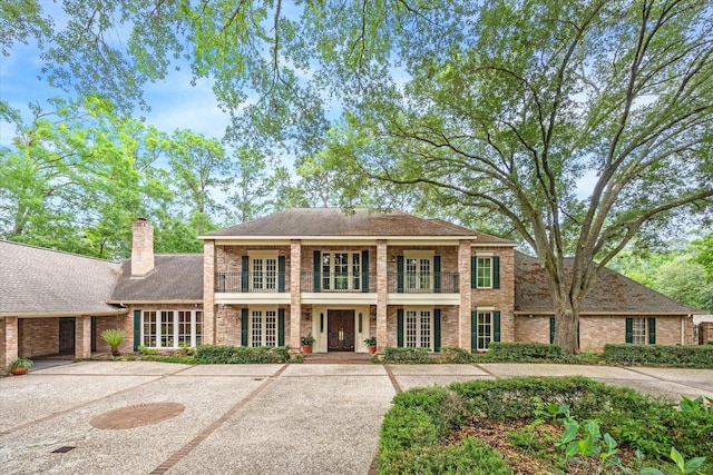 colonial-style house with brick siding, french doors, a balcony, and a chimney