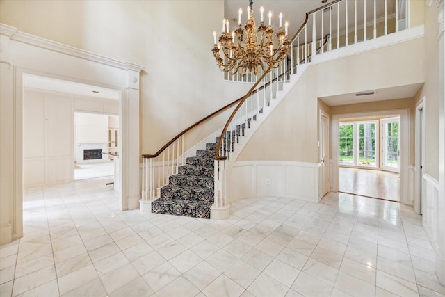 stairs with wainscoting, a towering ceiling, a decorative wall, and a notable chandelier