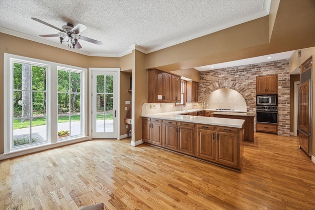 kitchen with brown cabinetry, a peninsula, oven, light countertops, and built in microwave
