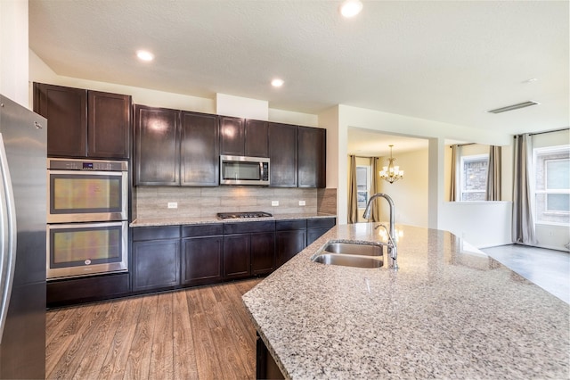 kitchen with a sink, stainless steel appliances, a chandelier, decorative backsplash, and dark brown cabinets