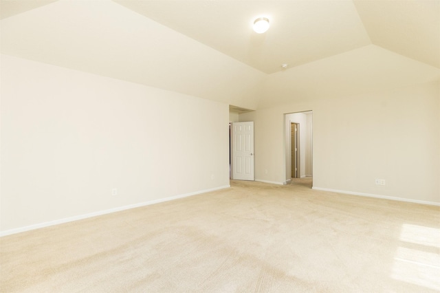 spare room featuring lofted ceiling, light colored carpet, and baseboards