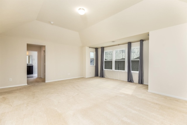 spare room with vaulted ceiling, light colored carpet, and baseboards