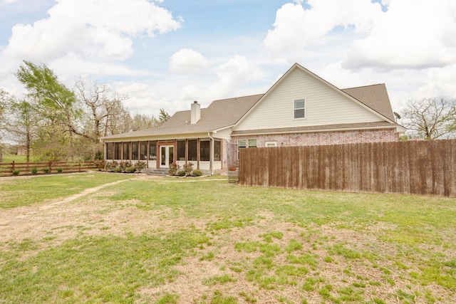 back of house featuring a fenced backyard, a chimney, a sunroom, brick siding, and a lawn