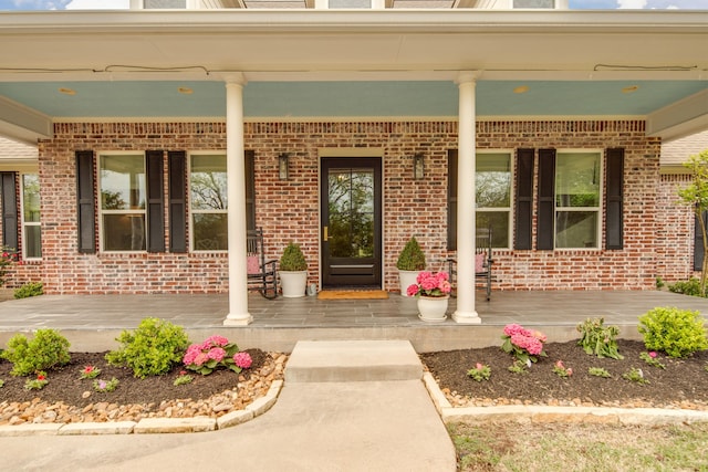 doorway to property with a porch and brick siding
