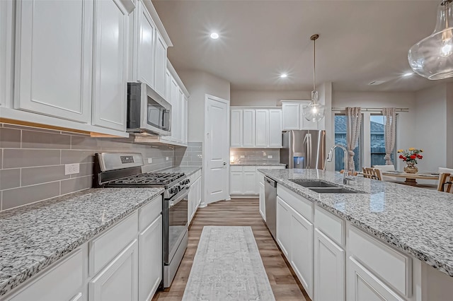 kitchen with white cabinets, a sink, light wood-style floors, stainless steel appliances, and tasteful backsplash