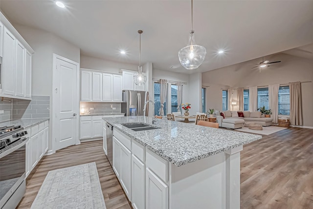 kitchen with a sink, white cabinets, light wood finished floors, stainless steel appliances, and an island with sink