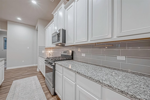 kitchen featuring light stone countertops, appliances with stainless steel finishes, light wood finished floors, white cabinetry, and baseboards
