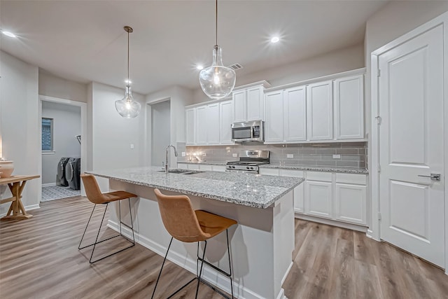 kitchen with washer and dryer, appliances with stainless steel finishes, a sink, light wood-style floors, and tasteful backsplash