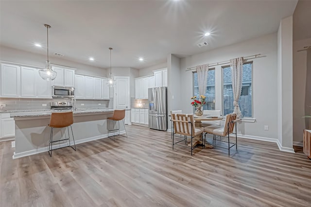 kitchen featuring a center island with sink, backsplash, white cabinets, and stainless steel appliances
