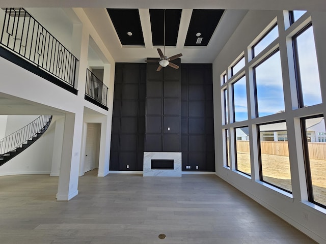 unfurnished living room featuring light wood-style floors, baseboards, a towering ceiling, and ceiling fan
