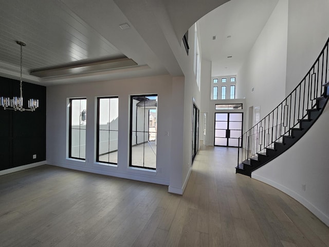 foyer entrance with baseboards, a raised ceiling, wood finished floors, and a chandelier