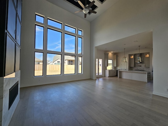 unfurnished living room featuring a ceiling fan, a towering ceiling, dark wood-style floors, and a fireplace