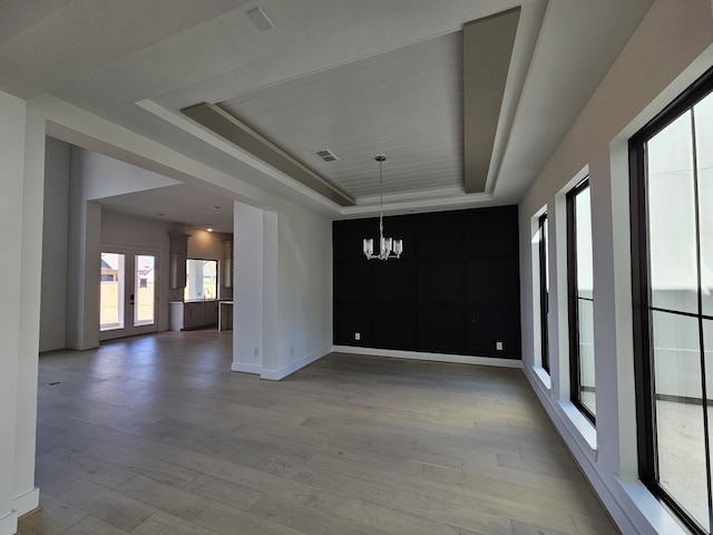unfurnished dining area with visible vents, baseboards, light wood finished floors, a notable chandelier, and a tray ceiling