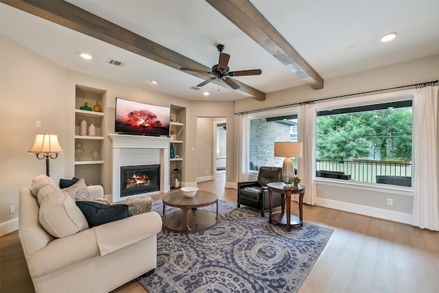 living room featuring a glass covered fireplace, baseboards, beamed ceiling, and wood finished floors