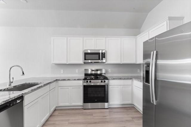 11869 E Gate Dr, Willis, TX 77318 - kitchen featuring lofted ceiling, light stone countertops, white cabinets, a sink, and appliances with stainless steel finishes
